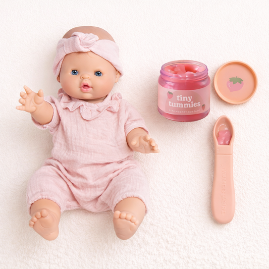 Coffret cadeau avec poupon Charlotte rose, petit pot fraise Tiny Tummies et cuillère sur fond crème