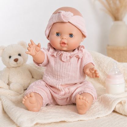 Poupon Charlotte rose assis sur un plaid crème avec ours en peluche et biberon sur fond clair
